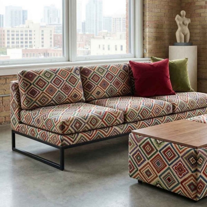 Trzyosobowa sofa na czarnej metalowej konstrukcji oraz dopasowana pufa, obite żakardową tkaniną Diego w geometryczny, aztecki wzór z motywem kolorowych rombów. Na kanapie leżą dekoracyjne poduszki w kolorze bordowym i oliwkowym.