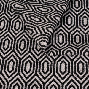 Zbliżenie na strukturę tkaniny tapicerskiej o wzorze geometrycznym. Czarno białe, kontrastowe linie tworzą wzór wydłużonych sześciokątów (heksagonów) na jasnoszarym, melanżowym tle.