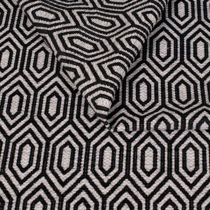 Zbliżenie na strukturę tkaniny tapicerskiej o wzorze geometrycznym. Czarno białe, kontrastowe linie tworzą wzór wydłużonych sześciokątów (heksagonów) na jasnoszarym, melanżowym tle.