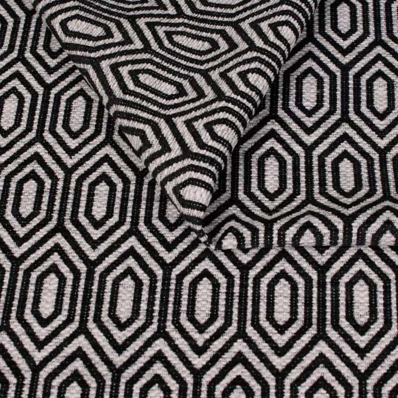 Zbliżenie na strukturę tkaniny tapicerskiej o wzorze geometrycznym. Czarno białe, kontrastowe linie tworzą wzór wydłużonych sześciokątów (heksagonów) na jasnoszarym, melanżowym tle.